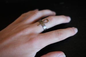 a picture of a sterling silver ankh ring on a finger. dark background