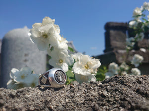 sterling silver japanese kamon ring with triforce design on a temple wall. plum blossoms and  japanese temple in background.